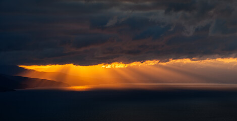 Panoramic view of sunset with orange sun rays through dark clouds