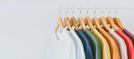 close up collection of colorful t-shirts hanging on wooden clothes hanger in closet or clothing rack over white background, copy space - obrazy, fototapety, plakaty