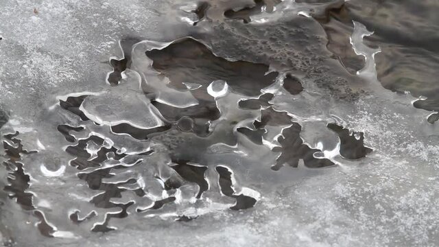 water flows slowly under the openwork blurred surface of the ice
