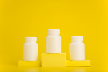 White medication bottles on winner pedestal against yellow background. Minimalistic creative concept of healthcare with a space for text