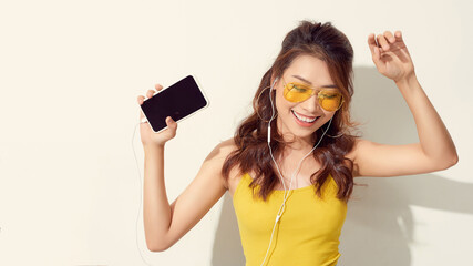 Happy carefree young woman dancing and listening to music from smartphone over white background
