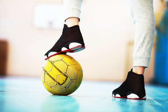 A human foot rest on the football on the concrete floor. Photo of one soccer ball and sneakers in a wooden floor.