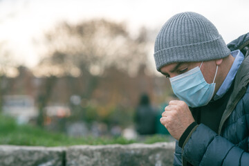 Prevent the spread of the Coronavirus Disease 2019 (COVID-19). Man in park sneezing or coughing into a protective medical face mask