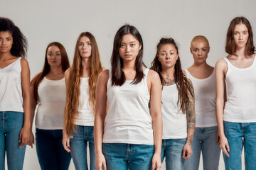 Portrait of beautiful young asian woman in white shirt looking at camera. Group of diverse women posing, standing isolated over grey background
