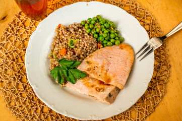 Plate with turkey meat, buckwheat and carrot, pea and leaf, fork and glass of drink.