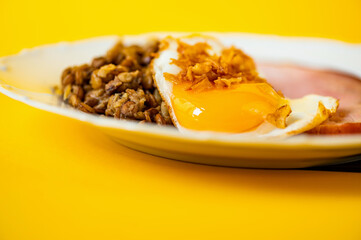 Fried egg with onion, boiled lentil and smoked meat on white plate on yellow background, copy space.