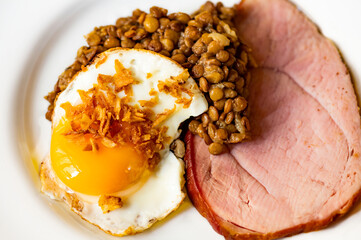 Smoked meat, fried egg with onion and boiled lentil on white plate