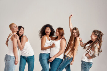 Group of six beautiful diverse young women wearing white shirt and denim jeans having fun, laughing...