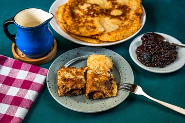 Fried potato pancake on 2 plate with cutlery, blue  pitcher, plum jam and towel on green table, closeup
