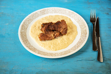 Plate with horseradish sauce and baked beef from peeled shoulder (clod) on blue table, cutlery.