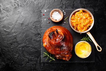 Roasted pork knuckle with braised boiled cabbage and mustard on black background. Flat lay.