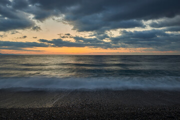 the first lights of dawn a beautiful autumn day and draw reflections on the clouds of the sky that become colorful, while the waves on the pebble beach are confused by long exposure