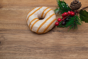 Donut in glaze and festive pine branch on wooden natural background