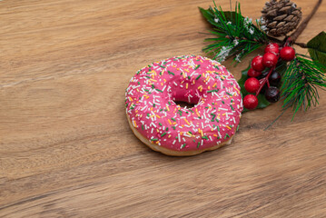 Pink Donut in glaze and festive pine branch on wooden natural background