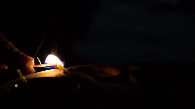 Minimal slow motion shot on black of matchstick being used to light a diya oil lamp with cotton wick dipped in oil on the indian festival of diwali bringing light to the very dark frame showing how