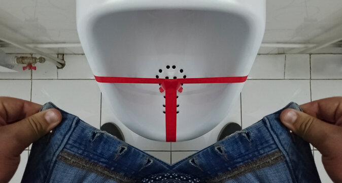 Man pissing in the pissoir (urinal), top view. Young adult  man pulls up his blue jeans.fly unbuttoned pants