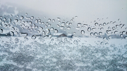 rain drops and snow on a window in a winter landscape with a house in the background in Lenk, Switzerland
