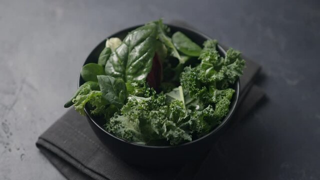 The girl pricks a salad leaf on a fork. The camera pans over the salad plate. Dark background