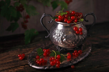 Still life with red currant in a vintage vase on a wooden table.