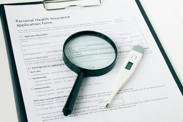 A magnifying glass and an electronic thermometer lie on the health insurance form