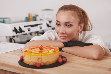 Gorgeous young woman looking at freshly made raw vegan cake she is selling at her coffee shop