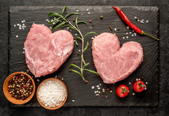 two raw pork steaks in the shape of a heart with spices for Valentine's Day on a stone background