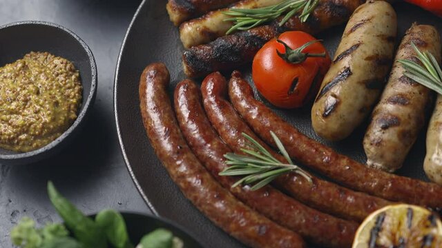 A dish of grilled sausages, tomatoes, lemon, vegetables. Fresh salad, dark background. The camera moves to the dish