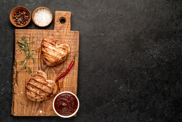 Obraz na płótnie Canvas two grilled pork steaks in the shape of a heart with spices for Valentine's Day on a stone background with place for text. dinner concept for two for valentine's day celebration