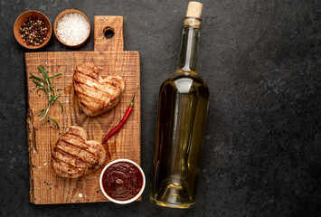 two grilled pork steaks with heart shaped spices, a bottle of white wine for Valentine's Day dinner on a stone background with copy space for your text