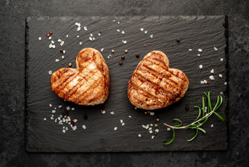 two heart shaped grilled pork steaks with spices for valentines day on stone background. dinner concept for two for valentines day celebration