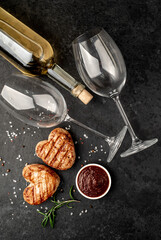 two grilled pork steaks with heart shaped spices, a bottle of white wine with two glasses for Valentine's Day dinner on a stone background
