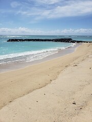 sandy beach by the sea with a rocky breakwater against the blue sky