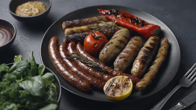 Dish with grilled sausages with smoke, grilled vegetables, lettuce, barbecue, camera moves forward, dark background