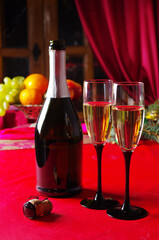 Two glasses of champagne, a bottle on Christmas, and a table with a red tablecloth.