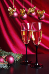 Two glasses of champagne, a decorated Christmas tree against a background of burgundy drapery.