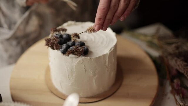 Chef decorates a cake with berries and dried flowers. Woman making cake at kitchen workplace. Unsurpassed pre-holiday atmosphere and home comfort. Homemade bakery concept