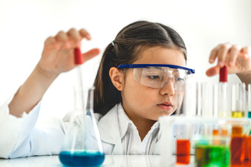 Cute little girl student child learning research and doing a chemical experiment while making analyzing and mixing liquid in glass at science class on the table.Education and science concept