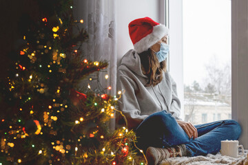 a young woman sits on the window in a decorated house for Christmas, sorts out the window, a woman in a medical sterile mask