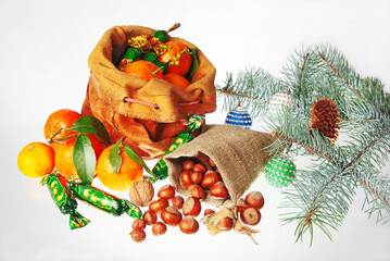 Saint Nicholas day gifts, isolated on white, bag with tangerines, sweets, bag with nuts, burning candle, fir branch and Christmas tree decorations.