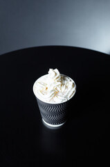 Disposable paper cup with tasty coffee drink with milk and whipped cream on wooden table in cafe. Selective focus, blurred background