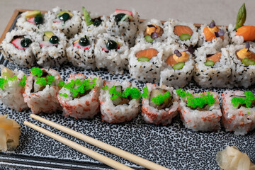 close up of an assortment of delicious uramaki with out of focus pickled ginger and chopsticks