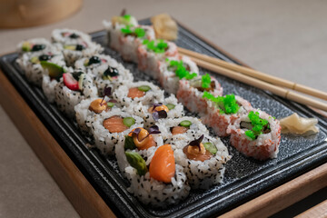 an assortment of uramaki pieces with out of focus chopsticks and pickled ginger on a tray