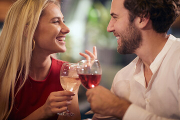 Fototapeta na wymiar beautiful caucasian couple in love, celebrating, toasting with wine, looking each other, smiling.