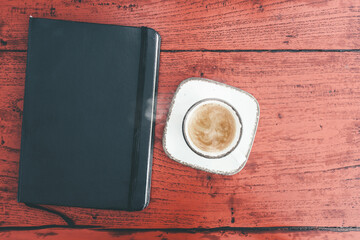 directly above view of steaming hot cup of espresso and diary on rustic red wooden table