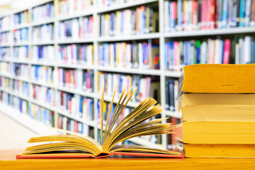 A pile of books and open book with blurred library bookshelf as background and copy space