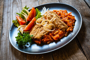 Fish dish - fried fish fillet on vegetable sauce on wooden table

