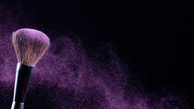 Makeup brush shudders and creates a swirl of fine particles of pink powder against a black background, slow motion, 300fps