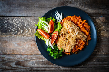 Fish dish - fried fish fillet on vegetable sauce on wooden table
