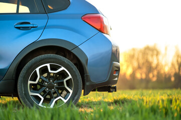 Close up of blue off road car on green grass. Traveling by auto, adventure in wildlife, expedition or extreme travel on a SUV automobile. Offroad 4x4 vehicle in field at sunrise.