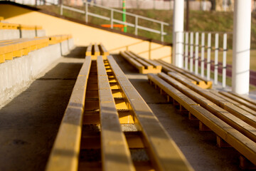 Outdoors gymnasium or stadium section, yellow painted wooden empty benches on sunny summer day. Sport and recreation concept.